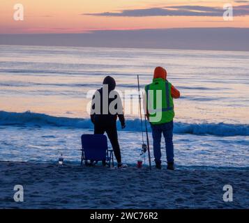 Deux individus se tiennent au bord d'une plage de sable, leurs regards fixés sur la vaste étendue d'océan bleu scintillant devant eux Banque D'Images