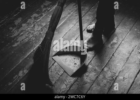 Les pieds des femmes sur le sol et un balai et une pelle à poussière à proximité, une fille balayant le sol de la maison, photo noir et blanc, nettoyage Banque D'Images