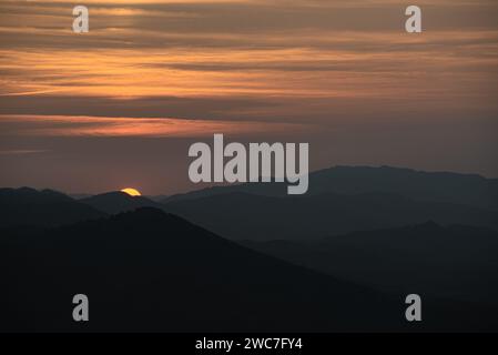 Un coucher de soleil à couper le souffle projette une lueur chaude sur les collines et les vallées pittoresques au loin, créant une scène sereine et idyllique Banque D'Images