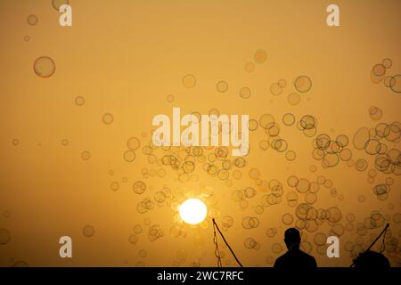 Un homme en silhouette fait beaucoup de bulles de savon avec un bâton de bulles de savon, elles flottent dans le ciel orange au coucher du soleil Banque D'Images