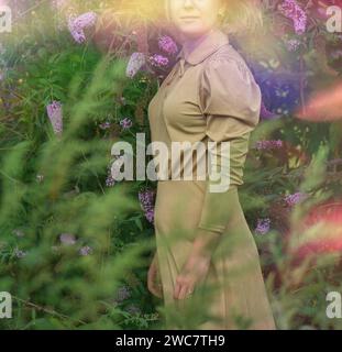 Bonne femme dans la bourddleia fleurs champ dans la luxueuse robe d'or.Jeune femme en robe d'or debout dans le champ de fleurs. Banque D'Images