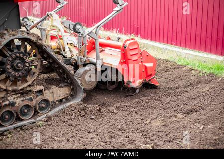 un tracteur caterpillar équipé d'une débroussailleuse aspire le sol d'un terrain de jardin. Banque D'Images