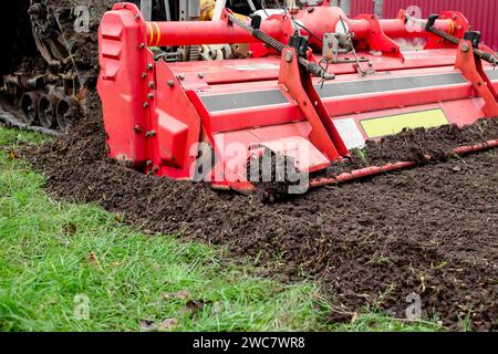 un tracteur caterpillar équipé d'une débroussailleuse aspire le sol d'un terrain de jardin. Banque D'Images