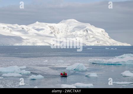 Zodiac naviguant à travers la glace à Neko Harbor, Antarctique, de l'eau remplie de glace et des icebergs échoués sur place, des reflets et des sommets enneigés Banque D'Images