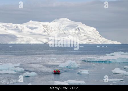 Zodiac naviguant à travers la glace à Neko Harbor, Antarctique, de l'eau remplie de glace et des icebergs échoués sur place, des reflets et des sommets enneigés Banque D'Images