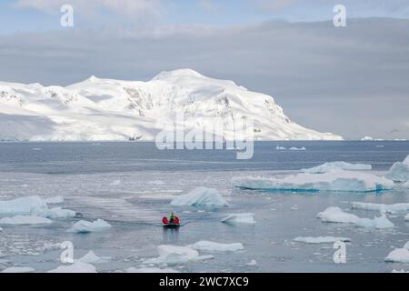 Zodiac naviguant à travers la glace à Neko Harbor, Antarctique, de l'eau remplie de glace et des icebergs échoués sur place, des reflets et des sommets enneigés Banque D'Images