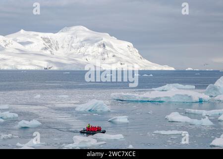 Zodiac naviguant à travers la glace à Neko Harbor, Antarctique, de l'eau remplie de glace et des icebergs échoués sur place, des reflets et des sommets enneigés Banque D'Images