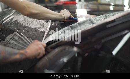 Film de protection pour l'application professionnelle la voiture rouge. Colles maître un film de protection sur le capot de la voiture Banque D'Images
