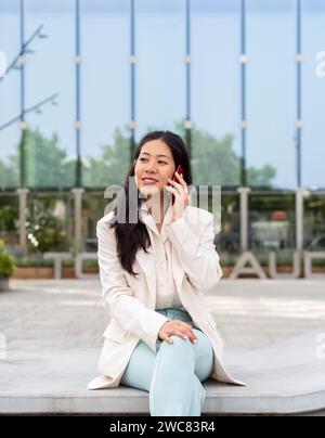Femme d'affaires asiatique parlant sur smartphone dans un quartier financier Banque D'Images