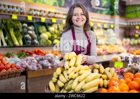 Jeune vendeuse tenant des bananes debout près du comptoir dans le marché d'épicerie Banque D'Images