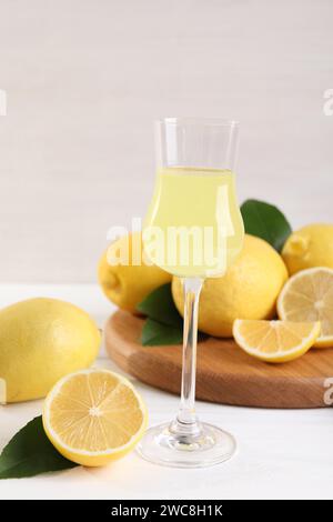 Verre à liqueur avec limoncello savoureux, citrons et feuilles vertes sur une table en bois blanc Banque D'Images