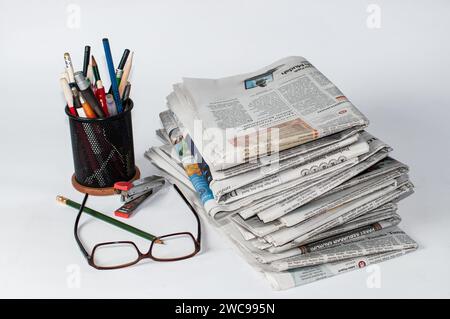 piles de journaux qui doivent être lus pour obtenir des informations sur les affaires et les nouvelles financières, plus papeterie et lunettes sur la table Banque D'Images