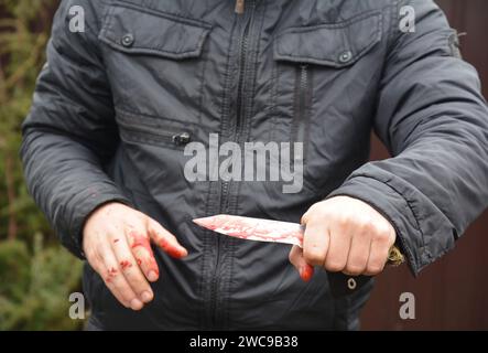 Photo d'attaque au couteau. Meurtrier, le tueur attaque avec un couteau avec des gouttes de sang rouge sur les mains. Banque D'Images