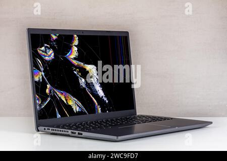 ordinateur portable avec un écran cassé dans les fissures et avec des cristaux qui fuient sur un fond gris gros plan Banque D'Images