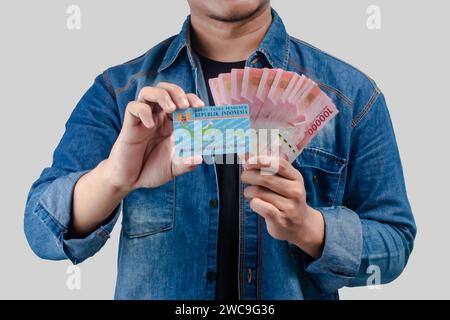 Jeune homme asiatique tenant du papier-monnaie et une carte d'identité regardant la caméra Banque D'Images