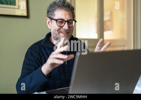 Homme mature avec une expression joyeuse s'engageant dans un appel vidéo animé sur son ordinateur portable. Banque D'Images