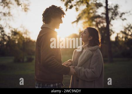 Portrait d'heureux couple amoureux dans le parc au coucher du soleil. Couple en silhouette se regardant l'un l'autre. Banque D'Images