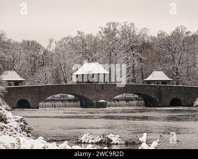 Un pont de pierre traverse une rivière tranquille entourée d'arbres enneigés. Leipzig, Allemagne Banque D'Images