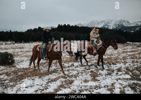 Papa monte à cheval, tirant l'arbre ; maman tient bébé dans un voyage festif Banque D'Images