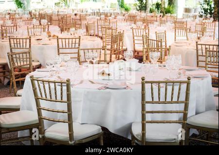 Tables rondes avec nappes blanches et verrerie servie avec chaises dorées placées à l'extérieur avant la célébration de l'événement Banque D'Images