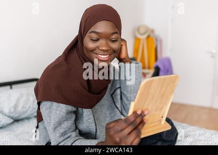 Heureuse femme africaine regardant le miroir tout en mettant le foulard musulman à la maison Banque D'Images