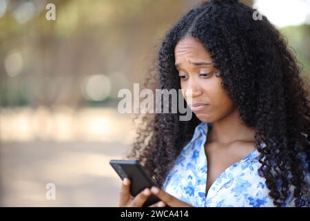 Femme noire déçue vérifiant le téléphone portable dans un parc Banque D'Images