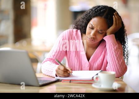 Étudiant inquiet étudiant à prendre des notes dans une terrasse de restaurant Banque D'Images