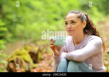 Femme buvant du café et contemplant assise dans une forêt Banque D'Images