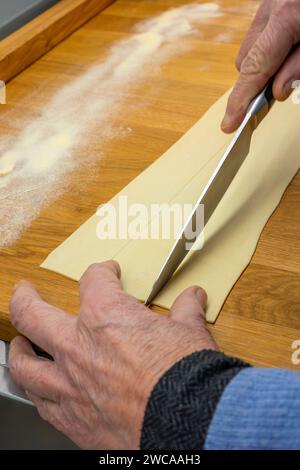 Production de pâtes faites maison - nouilles italiennes à faire soi-même - gros plan des mains qui coupent la pâte enroulée pour préparer des pâtes faites soi-même Banque D'Images