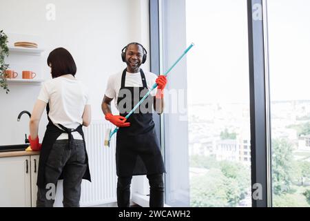 Ouvrier masculin africain lave les fenêtres, s'amusant tout en tenant une vadrouille comme une guitare. Banque D'Images