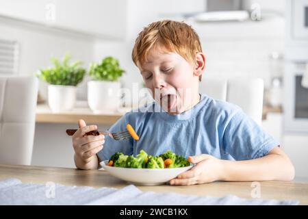 Le petit garçon regarde avec dégoût la carotte sur sa fourchette. Banque D'Images