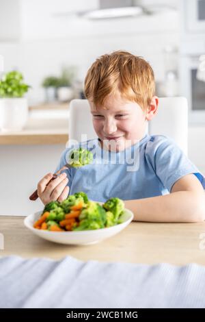 Le petit garçon regarde avec dégoût le brocoli sur sa fourchette. Banque D'Images