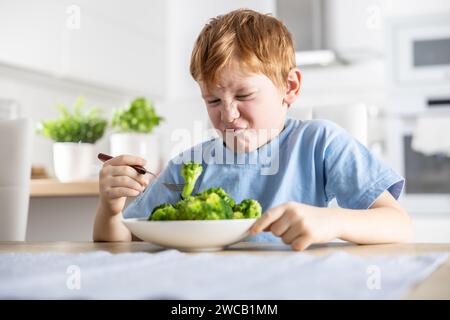 Le petit garçon regarde avec dégoût le brocoli sur sa fourchette. Banque D'Images