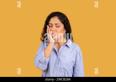 Femme avec une expression peinte, la main sur sa joue, les yeux fermés, souffrant peut-être d'un mal de dents Banque D'Images