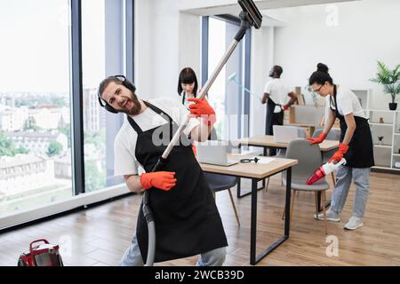 Heureuse équipe de personnes dans des tabliers noirs nettoyant le bureau moderne. Banque D'Images