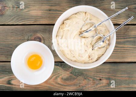 Pâte de l'accessoire de mélangeur et le jaune d'oeuf séparé du blanc pour la préparation des produits de boulangerie. Fond en bois, espace de copie. Banque D'Images