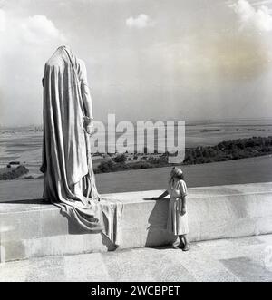 Années 1950, historique, une dame debout devant un mur de calcaire, regardant une sculpture, la Statue du Canada à deuil, sur la tombe de guerre de Vimy, en France. Situé sur le site de la victoire du Canada lors de la bataille de la crête de Vimy, le Mémorial de Vimy rend hommage aux Canadiens qui ont participé à la grande guerre, à la première Guerre mondiale, ainsi qu’à ceux qui sont morts sans tombe connue. Dévoilé par le roi Édouard VIII en 1936, le momument Vimy a été conçu par l'architecte et sculpteur canadien Walter Seymour Allward. Banque D'Images