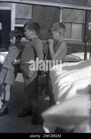 1942, historique, temps de guerre et trois patients, jeunes garçons, dehors près de leurs lits métalliques à l'hôpital pour enfants Queen Mary's Hospital, Carshalton, Surrey, Angleterre, Royaume-Uni, un garçon a la main en plâtre. Banque D'Images