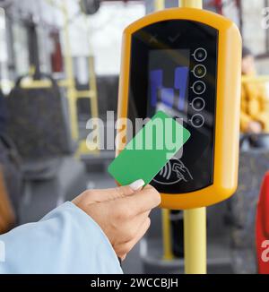 Récolte de la main féminine tenant la carte de paiement verte devant le validateur lors de l'embarquement dans un véhicule public. Vue rapprochée de la main à l'aide du terminal dans le transpor Banque D'Images