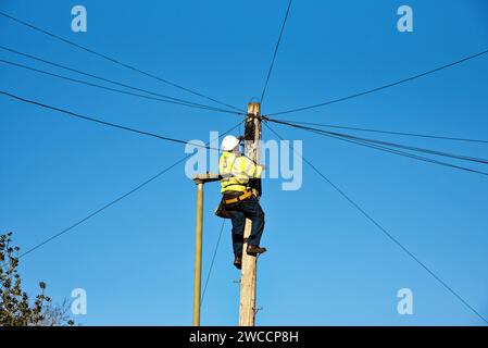 Un ingénieur téléphonique fixant le câblage sur le dessus d'un poteau de télégraphe Banque D'Images
