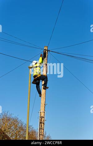 Un ingénieur téléphonique fixant le câblage sur le dessus d'un poteau de télégraphe Banque D'Images