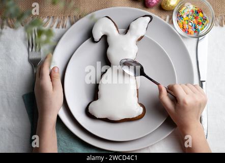 Vue de dessus d'un biscuit pain d'épice en forme de lapin. Mains d'enfant décorant biscuit avec cerise sur les vacances de Pâques Banque D'Images