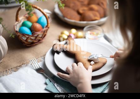 Mains d'enfant décorant des biscuits en pain d'épice avec cerise sur la table décorée festive à Pâques. Traditions de vacances, temps en famille Banque D'Images