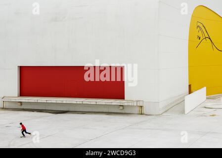 Un jeune garçon avec scooter et veste rouge au Centre moderne Niemeyer à Aviles, Asturies, Espagne. Banque D'Images