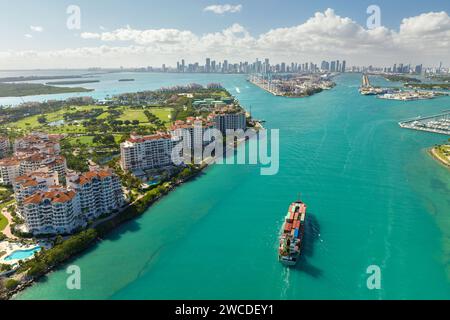 Navire porte-conteneurs commercial entrant dans le port de Miami par le canal principal près de South Beach. Hôtels luxueux et bâtiments résidentiels sur le front de mer Banque D'Images