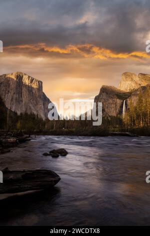 Un ciel de coucher de soleil dynamique et flamboyant qui brille sur l'emblématique vallée de Yosemite en Californie avec une rivière qui coule au premier plan. Banque D'Images