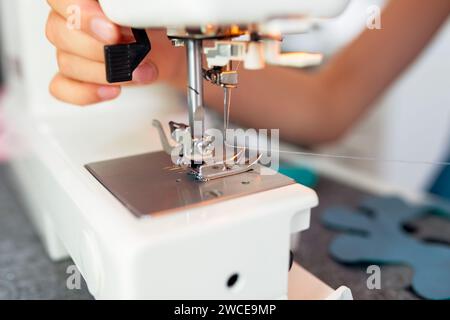Gros plan de la machine à coudre et de la main de couturière au travail. La fillette coud des vêtements sur la machine à coudre. Ateliers de confection créative pour enfants - conc Banque D'Images