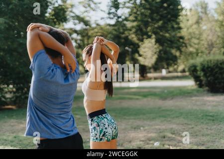 Un couple heureux fait de l'exercice en plein air dans un parc, profitant d'une journée ensoleillée. Ils s'étirent, s'échauffent et pratiquent diverses activités physiques. Banque D'Images