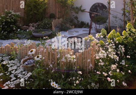 Une zone de gravier circulaire et un chemin de pierre entouré de poteaux de bambou, de murs blancs et d'aborder de fleurs blanches dans le jardin lunaire conçu par Queenie CH Banque D'Images