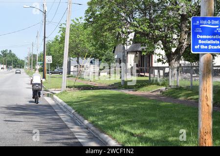 Bicyclisrts passe devant un panneau de rue Adoptez un parrainé par les socialistes démocrates des Ozarks - mai 2023 Banque D'Images